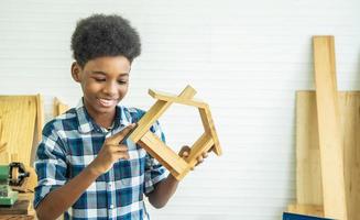 charpentier afro-américain souriant heureux de travailler avec une maison en bois et du papier de verre photo