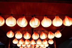 des lampes rouges tiennent sur un plafond et un éclairage en bois rouge, des rangées de lampes de style japonais. photo