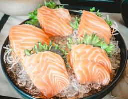 le sashimi se compose d'une tranche de poisson saumon cru placée sur la glace dans une tasse en céramique noire dans un restaurant. photo