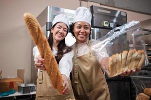 portrait de jeunes femmes chefs en uniformes de tablier avec des chapeaux regardant la caméra avec un sourire joyeux et fier avec du pain dans la cuisine. ami et partenaire des aliments de boulangerie et de l'occupation quotidienne de la boulangerie fraîche.