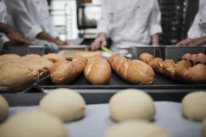 gros plan et mise au point sélective sur des baguettes et du pain délicieux devant l'équipe de chefs en uniforme blanc, pétrir la pâte à pâtisserie crue, préparer des aliments de boulangerie frais, cuire au four dans la cuisine du restaurant. photo