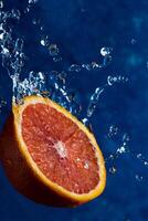 une demi-orange tombe sur un fond bleu avec des gouttes d'eau photo