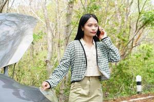 une femme asiatique appelle un mécanicien, la voiture sort sur la route autour de la forêt. photo