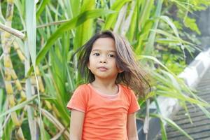 expression heureuse petite fille indonésienne aux cheveux lâches sur fond de canne à sucre photo