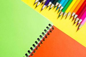 palette arc-en-ciel de crayons de couleur avec un cahier à spirale sur fond jaune, maquette, mise à plat. rentrée scolaire, recrutement étudiant, artiste, cours de dessin. espace de copie. papeterie pour la créativité