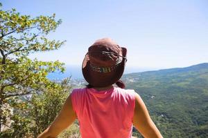 femme au chapeau regarde la vue panoramique de la montagne à la mer et à la forêt. tourisme, trekking, voyage. écotourisme actif, mode de vie sain, aventure photo