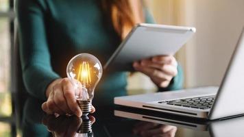 femme d'affaires utilisant un smartphone, une tablette et tenant une ampoule, avec une idée d'innovation et de créativité