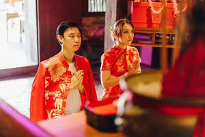 heureux jeune couple asiatique en robes traditionnelles chinoises priant au temple photo