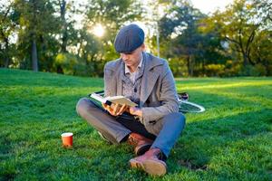 jeune homme hipster lire un livre dans le parc d'automne photo