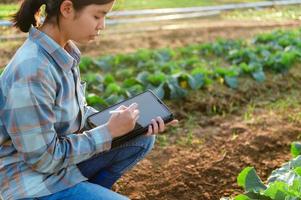 une femme asiatique utilise une tablette pour vérifier les informations sur la culture des légumes dans le jardin photo