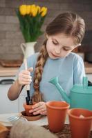 petite fille assise à la table à la maison, semant des graines dans des pots de fleurs. photo