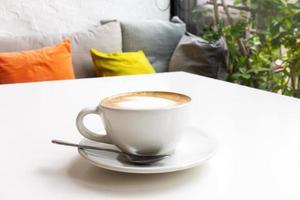 café chaud sur la table blanche dans le café près du canapé et de la fenêtre en verre. photo