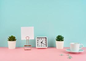 maquette avec cadre blanc, note, alarme, tasse de café ou de thé sur une table rose contre un mur bleu