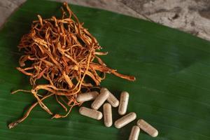 Cordyceps militaris sec sur une feuille de banane verte avec fond en bois. champignon médical orange pour une bonne santé avec des capsules. photo