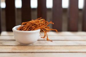 mycélium cordyceps militaris sec dans un bol blanc avec fond en bois. champignon médical orange pour une bonne santé. photo