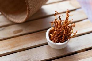 mycélium cordyceps militaris sec dans un bol blanc avec fond en bois. champignon médical orange pour une bonne santé. photo