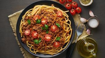 pâtes bolognaise bucatini avec viande hachée et tomates, fond en bois foncé, vue de dessus, bannière longue photo