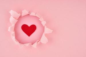 Saint Valentin. un trou déchiré et un coeur rouge sur fond texturé rose vif, concept de papier déchiré avec espace de copie. bannière latérale longue largeur photo