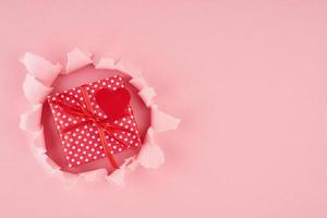 Saint Valentin. un trou déchiré et un coeur rouge avec une boîte cadeau en rose vif photo