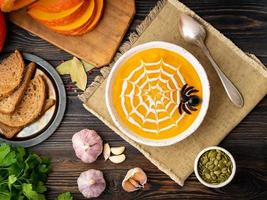 nourriture drôle pour halloween. soupe de purée de citrouille, toile d'araignée, vieille table en bois sombre, vue de dessus. photo