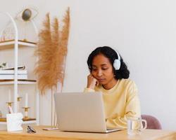 Étudiante afro-américaine endormie dans des écouteurs assistant à une conférence en ligne sur un ordinateur portable à la maison