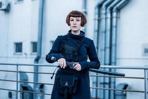 portrait d'une jeune femme rousse avec une épée japonaise vêtue d'un costume cyberpunk futuriste debout sur le toit. photo