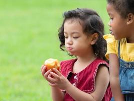 un groupe de jeunes enfants de nombreuses nationalités jouent et mangent des fruits en dehors de l'école photo