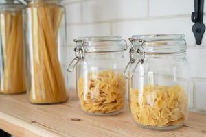 pâtes italiennes de blé dans un bocal en verre sur une étagère en bois dans la cuisine. photo