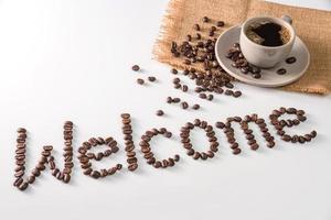 tasse à café et texte en grains de café, isolés sur blanc. texte le mot bienvenue fait de grains de café. Police de caractère photo