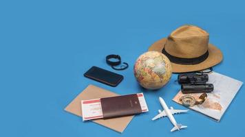 vacances de planification touristique à l'aide de la carte du monde avec d'autres accessoires de voyage autour. smartphone, appareil photo argentique et lunettes de soleil sur fond bleu.