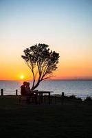 scène romantique avec un couple assis ensemble et regardant le magnifique coucher de soleil sur la plage de brighton, en australie. photo