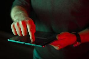 photo en gros plan d'un doigt d'homme touchant un écran de tablette numérique à la lumière rouge.