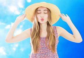 portrait de mode jolie femme en chapeau de paille d'été envoie un baiser d'air sur fond bleu frais photo