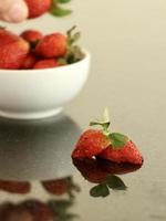 trancher la fraise sur une table de couleur inégale avec une main recadrée floue et une réflexion sur le dos. photo