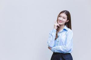 jeune femme d'affaires asiatique aux cheveux longs qui porte une chemise à manches longues bleue sourit joyeusement pendant qu'elle croise les bras pour présenter la pensée sur fond blanc. photo