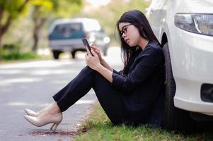 une jeune femme asiatique appelle son technicien de service pour réparer une voiture cassée sur le bord de la route