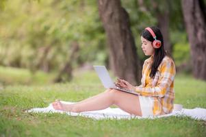 une belle femme asiatique se détend dans le jardin, lit et recherche des informations d'apprentissage sur Internet