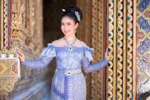 une belle et gracieuse femme thaïlandaise en robe thaïlandaise ornée de précieux bijoux se dresse dans un magnifique temple thaïlandais antique photo