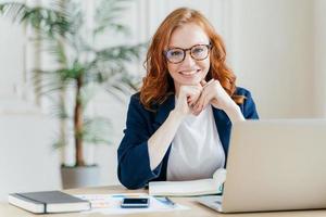 ravie et joyeuse, une économiste aux cheveux roux développe un projet de démarrage financier, pose à l'intérieur d'un bureau, travaille dans le domaine des affaires, vêtue de vêtements formels, a une expression heureuse, possède une entreprise photo