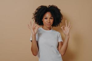 jeune femme afro-américaine gardant les deux mains dans un geste correct, isolée sur fond marron photo