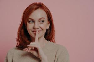 belle jeune femme gingembre souriante mettant le doigt sur les lèvres et faisant signe de silence photo