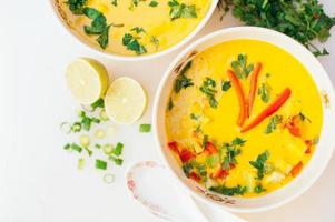 bol de soupe au curry frais avec poivron rouge, persil sur fond blanc. plat de légumes frais. deux tranches de citron vert près des bols de soupe. vue de dessus photo