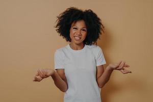 une femme africaine confuse ne peut pas prendre de décision, haussant les épaules isolée sur fond beige photo