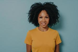 Portrait à la taille d'une femme métisse joyeuse aux cheveux bouclés posant en studio avec un sourire heureux photo