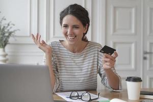 jeune femme italienne souriante effectuant un paiement avec une carte en plastique lors d'achats en ligne sur un ordinateur portable photo