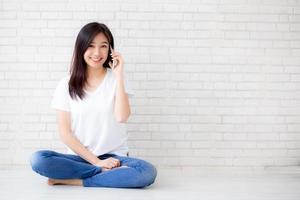 belle de portrait jeune femme asiatique parler téléphone intelligent et sourire assis sur fond de briques de béton de ciment, femme indépendante appelant le téléphone, communication du concept mobile. photo