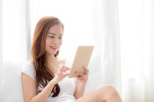 portrait d'une belle jeune femme asiatique tenant et lisant une tablette numérique avec loisirs, fille utilisant une tablette avec détente dans la chambre, style de vie et concept de communication. photo