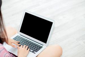 portrait d'une belle jeune femme asiatique assise à l'aide d'un ordinateur portable dans le salon pour les loisirs et la détente, indépendante avec un cahier de travail de fille, un concept de communication et de style de vie. photo
