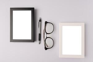 cadre photo noir, cadre photo blanc, lunettes et stylo sur fond blanc