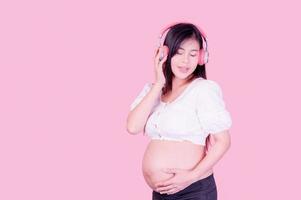 belle femme enceinte asiatique se tient détendue et aime écouter de la musique sur des écouteurs connectés à internet photo